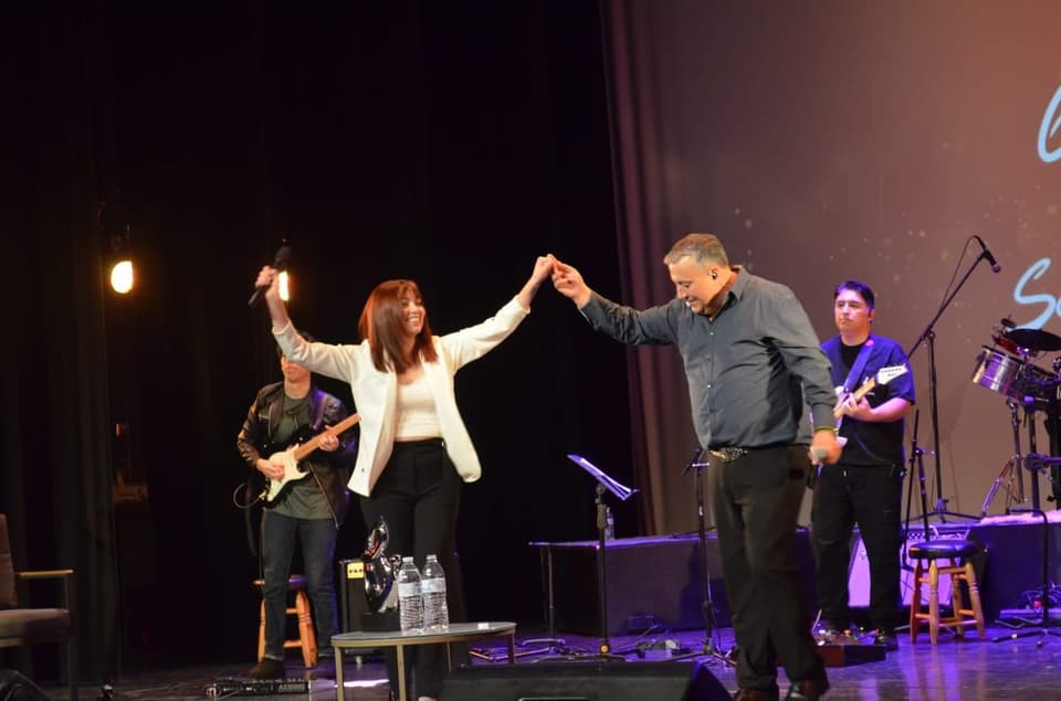 Vocalista bailando con una invitada en el escenario de un teatro, con la banda tocando atrás
